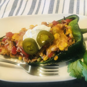 Vegetarian stuffed poblano sitting on a white plate next to a silver fork